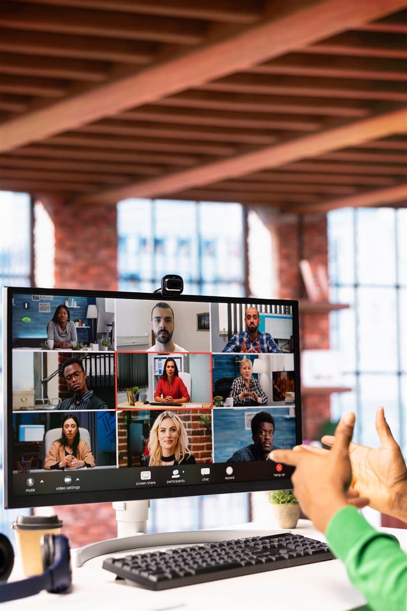 Hands gesturing toward a video conference on a large monitor